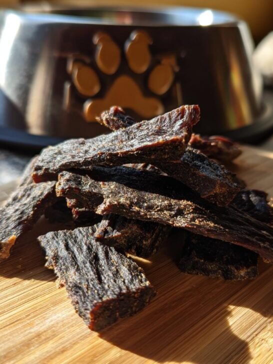 A pile of homemade Beef Carob Safe Treat Jerky for dogs on a wooden cutting board.
