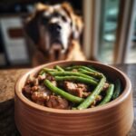 A wooden bowl filled with a hearty Beef and Green Bean Protein Mix, with a dog in the background.