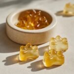 Close-up of golden, paw-shaped Calcium Boost Bone Broth Gummies for Dogs, with more in a small bowl.