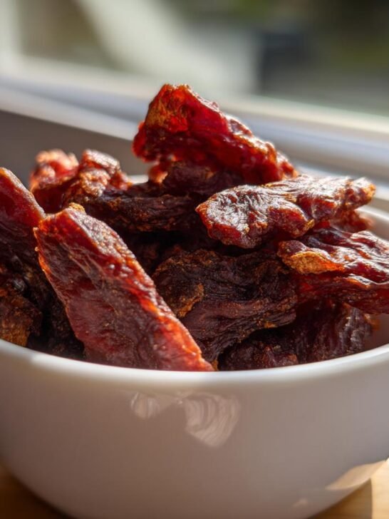 A white bowl filled with homemade Chicken Blueberry Energy Jerky, bathed in sunlight.