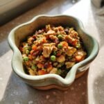 A close-up of a Chicken and Green Pea Bowl, featuring chopped chicken, peas, carrots, and other ingredients in a decorative bowl.