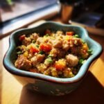 A close-up of a bowl filled with a healthy Chicken and Quinoa Strong Body Meal, featuring chicken pieces, quinoa, peas, and carrots.