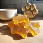 Pile of translucent, amber-colored bone-shaped Happy Belly Bone Broth Gummy Bones for Dogs on a wooden surface.