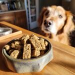 A bowl filled with Homemade Turkey and Carrot Dry Bake Protein Kibble, with a golden retriever looking eagerly in the background.
