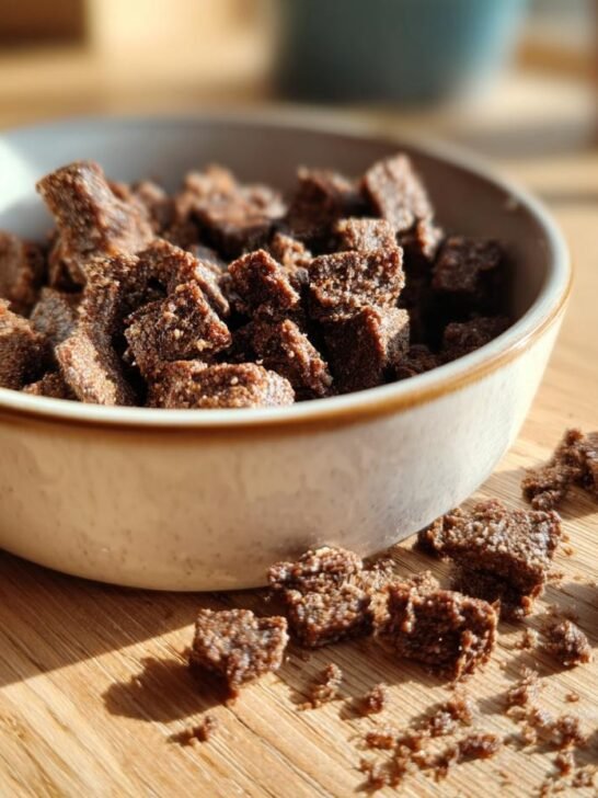 Close-up of dark, textured pieces of Homemade Turkey and Zucchini Low Fat Kibble Mix in a small bowl.