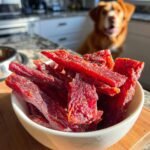 A white bowl filled with homemade Turkey Ginger Immunity Jerky, with a dog in the background.