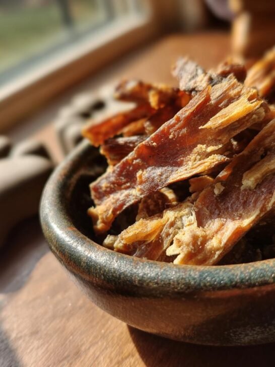 Close-up of Turkey Oat Digestive Jerky strips in a rustic bowl, bathed in sunlight.